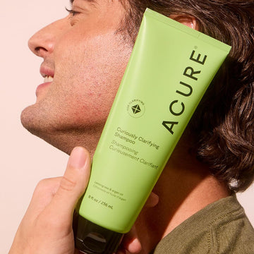 Frasco con hierba limón y Acure Curiously Clarifying Shampoo para refrescar el cuero cabelludo.