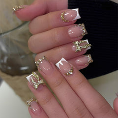 Uñas francesas con lazo dorado de Tnbuokas, estilo elegante para cualquier ocasión.